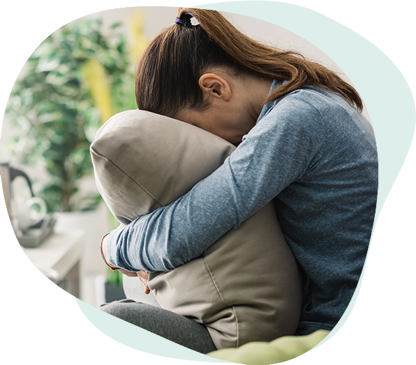 woman struggling with anxiety or other issues hugging a pillow burying her face in it.